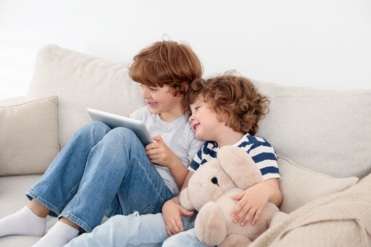 Cute little brothers with tablet on sofa at home