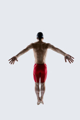 Full length rear view. Muscular swimmer rotates torso and lifts one arm in fluid stroke twist showing dynamic motion against white studio background. Concept of sport training, movement