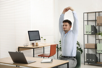 Handsome man stretching on chair in office