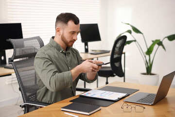 Man taking photo of document using scanning app on smartphone at desk in office
