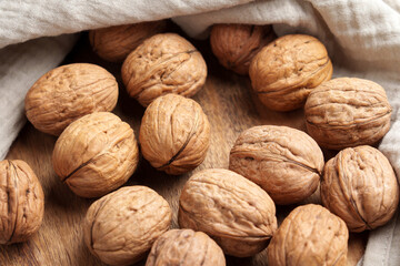 Pile of whole unshelled walnuts on wooden table with crumpled cloth napkin. Top view