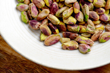 Shelled roasted pistachio nuts in plate on wooden table close up