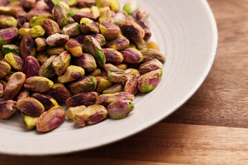 Pile of peeled pistachio nuts in kitchen bowl on wooden table. 