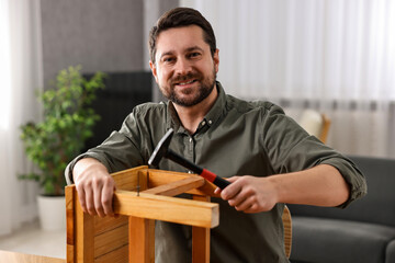 Man repairing wooden stool with nail and hammer at home