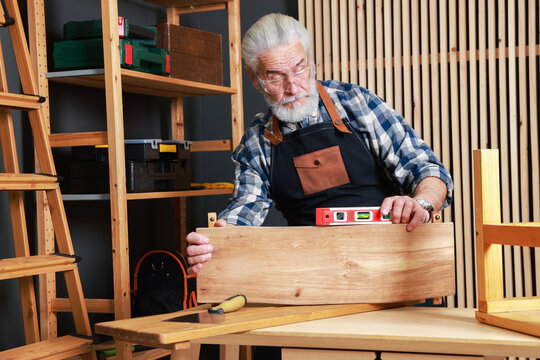 Relaxing hobby. Senior man working with wooden plank and level tool at table in workshop