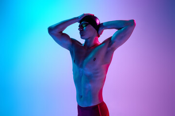 Athletic man, swimmer adjusts goggles with calm expression and intense gaze in vibrant neon light against gradient background. Concept of sport, active and healthy lifestyle, competition, training