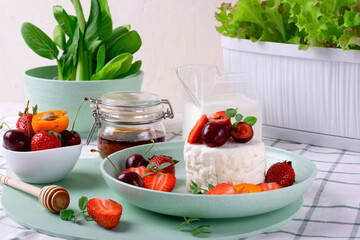 Homemade ricotta cheese served with strawberry, cherry, apricot and honey on light green plate. Italian cuisine