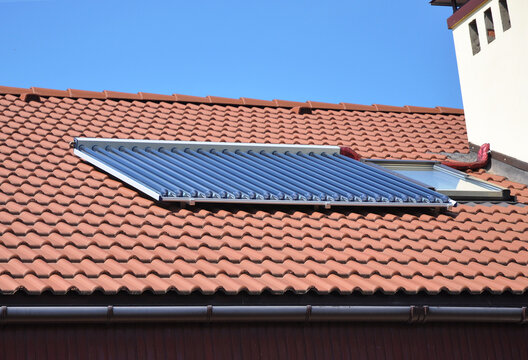 House rooftop solar water heating (SWH) is heating water by sunlight, using a solar thermal collector. House red clay tiles roof with solar water heating panel and attic skylights windows
