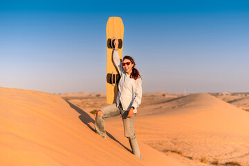 Young woman enjoying the thrill of sandboarding in the sun soaked desert of Dubai, United Arab Emirates, surrounded by stunning dunes