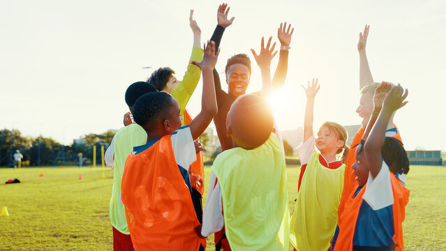 Hands up, soccer and coach in huddle with happy kids on field for motivation, game plan or strategy. Excited, training and practice with children in celebration for sports, football player or support