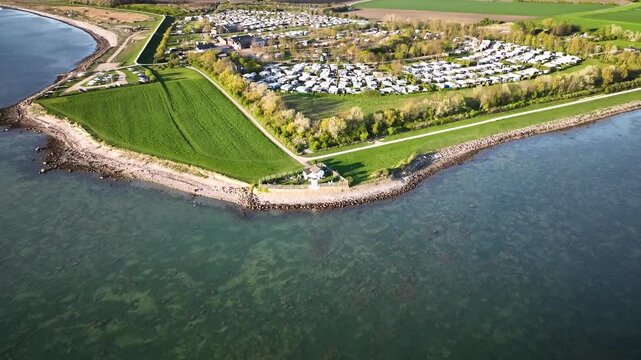 Aerial footage of the Strukkamphuk lighthouse on the Baltic Sea island of Fehmarn with a coastal campground. Forward fly with tilt down over Strukkamphuk lighthouse.