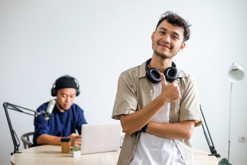 Asian Radio Host Showing Thumb Up and Smiling at Camera While Inside Broadcasting Studio