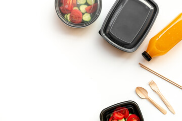 Tomatoes salad in lunch boxes with orange juice in a bottle and disposable cutlery, top view