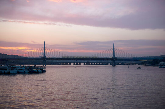 Sunset view of Halic Metro Bridge, or Golden Horn Metro Bridge, over the Golden Horn with boats and a colorful sky. Istanbul, Turkey