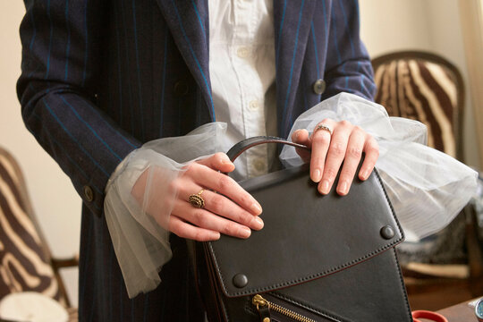 Close-up of woman in blue pinstripe suit holding a black leather handbag in an elegant setting. Germany