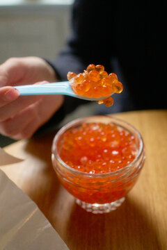 A spoonful of bright orange salmon roe above a glass bowl on a wooden table.
