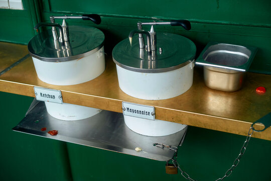 Stainless steel dispensers for ketchup and mayonnaise on a green background.