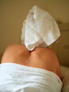 Woman relaxing with a towel on head and body wrapped in a towel, hotel spa setting ambiance.
