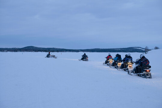 Snowmobiles travel across a vast snowy landscape under a cloudy sky. North Finland