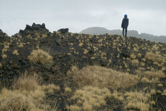 A lone hiker stands on a volcanic landscape under a cloudy sky. Sicily, Italy