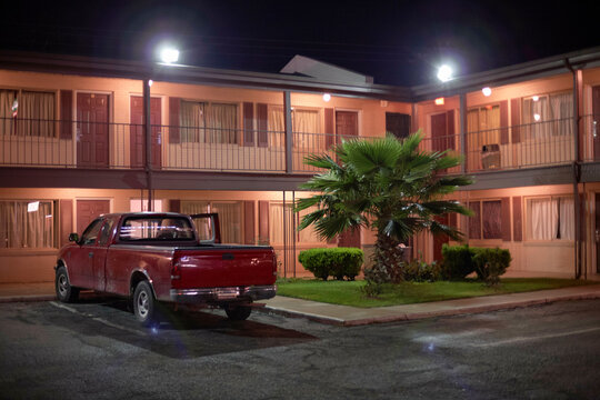 Night scene of a red pickup truck parked in front of a illuminated motel with a palm tree. Road Trip USA