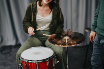A woman enthusiastically playing a drum set, captured in a music studio setting. Depicts artistic expression and passion for music with the vibrant red drum and focused energy.