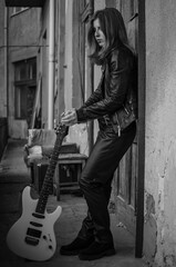Obraz premium Girl guitarist in leather jacket and leather pants with white electric guitar on city street Rock Style 