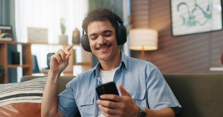 Phone, man and dancing with headphones on sofa for audio subscription, music playlist and weekend break. Relax, person and happy with internet connection in home for radio app, podcast or sound track