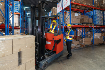 Two worker in safety gear collaborate inside a warehouse, one driving a forklift and the other reviewing inventory on a clipboard. Box are neatly stacked around them.