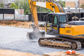 An excavator on a construction site in close-up. The excavator rams the crushed stone with a bucket for construction. Heavy machinery for construction and landscaping.