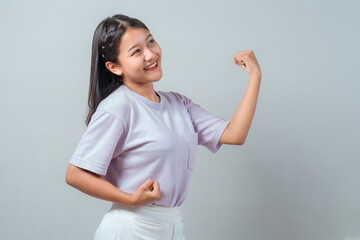 Smiling young Asian woman showing biceps with both arms, expressing strength and confidence. She...