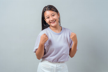 Cheerful young Asian woman smiling and raising both fists in a confident pose. She wears a pastel...