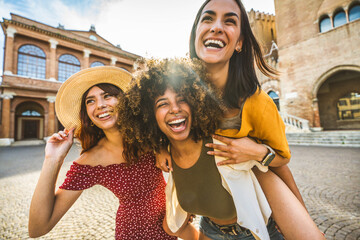 Multiracial young women having fun together walking in city street - Happy female friends enjoying summer vacation - Friendship concept with three beautiful girls laughing outdoors