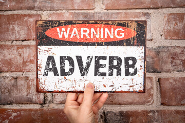 Adverb Warning Sign Held Against Brick Wall for Grammar Concept