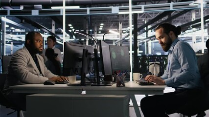 Panicked engineers in data center react to ransomware warning on PC display, scrambling to launch emergency response protocol. IT staff urgently trying to fix hacked infrastructure systems, camera A