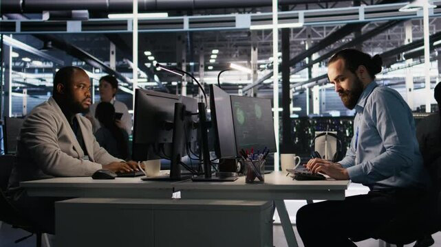 Panicked engineers in data center react to ransomware warning on PC display, scrambling to launch emergency response protocol. IT staff urgently trying to fix hacked infrastructure systems, camera A