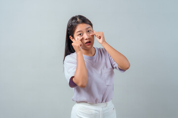 Young Asian woman making an expressive face while pulling down her lower eyelids with both hands....