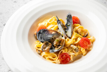 A gourmet seafood pasta dish with mussels, cherry tomatoes, and creamy sauce, served in a white bowl. The vibrant colors and fresh ingredients create an appetizing and elegant presentation