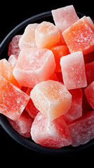 Vibrant gumdrop candies in various shades of red and pink are stacked together in a black bowl, showcasing their chewy texture and sweet appearance