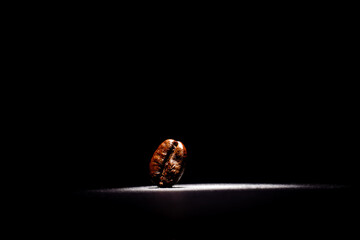 Minimalist close-up of a single roasted coffee bean on a black background with focused, bright lighting highlighting its rich texture and detail.


