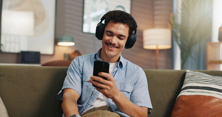 Headphones, man and relax with phone in home for streaming service, watching online video or weekend break. Happy, person and smartphone on sofa for audio playlist, music album or internet connection