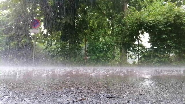 Heavy summer rain water drops falling into puddles on street pavement, 4K