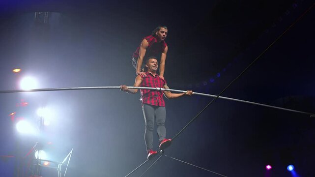 Circus show with tightrope walkers under dome of the circus under the light of spotlights and smoke.