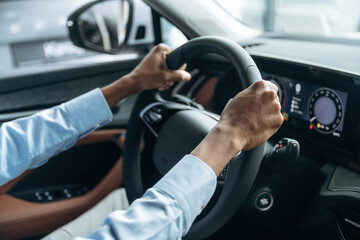 Hands are on the steering wheel. Man in shirt is in the modern car