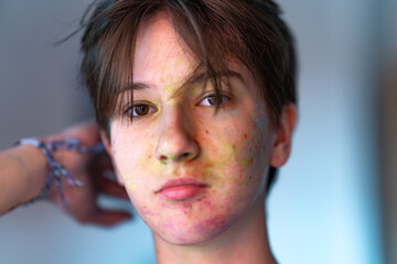 Conceptual soft focus portrait of a youth with abstract color splashes on the face, hand in the frame. Symbol of creative freedom, beauty in expression, and modern art.