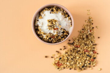 Granola with yogurt , high-resolution . Top view of a ceramic bowl with granola  and yoghurt on the light orange background . Muesli with dried fruit close-up , place for text . 