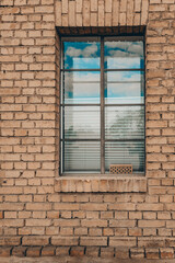 Reflections of clouds shimmer through a window framed by warm, textured brick in a peaceful rural setting during the afternoon