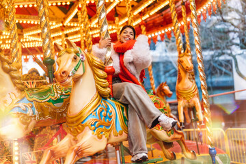 Joyful woman enjoys a festive carousel ride with illuminated horses at an amusement park during...