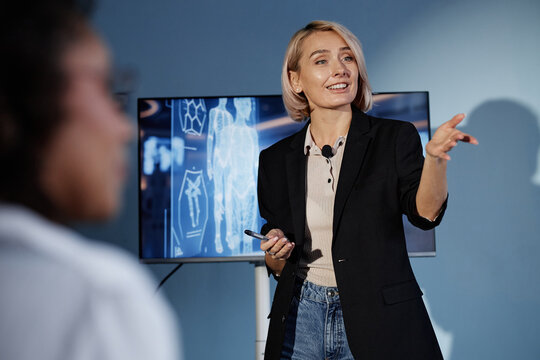 Female AI expert interacting with audience answering colleagues question while giving presentation on integrating innovative innovations into modern business in auditorium
