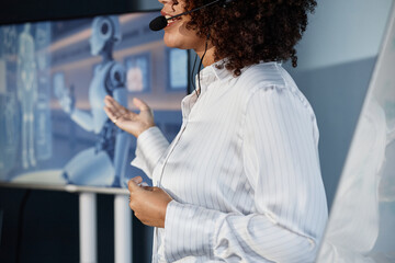 Cropped shot of female speaker wearing headset microphone leading talk on AI technology integration into modern business pointing at presentation on screen during professional conference